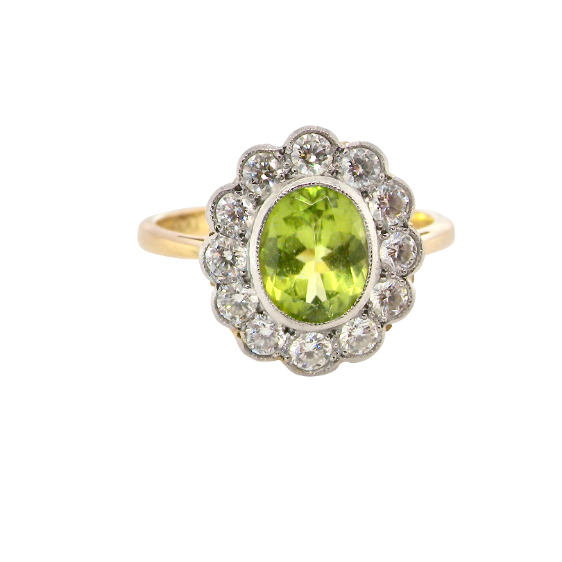 A vintage-style ring featuring an oval green peridot stone surrounded by a halo of small clear stones, set on a yellow gold band.