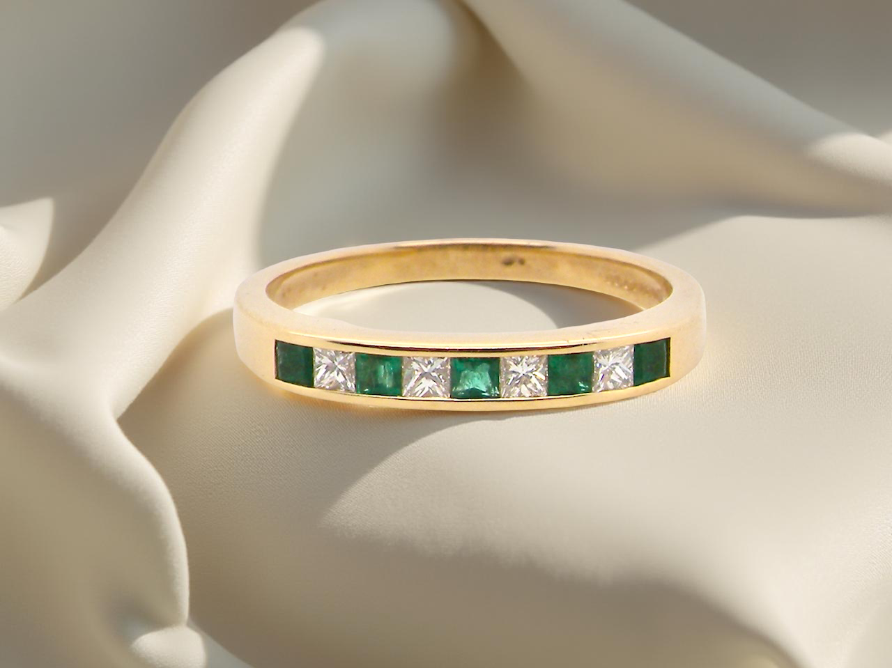 Gold ring with emeralds and diamonds on a soft fabric background