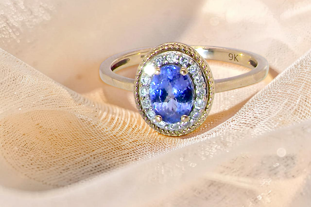 A 9 carat gold cluster ring. Features to the centre an oval cut tanzanite gem stone. Measures 7x5mm, claw setting.