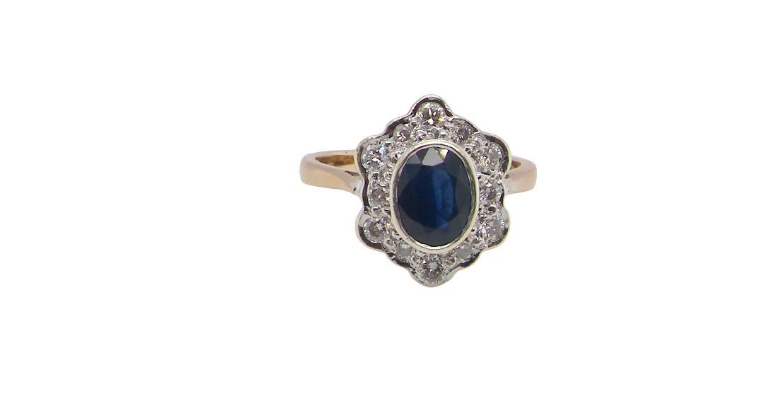 A 9 carat gold cluster ring that features an inky black blue oval cut sapphire. This measures 8x6mm in a safe rim style setting