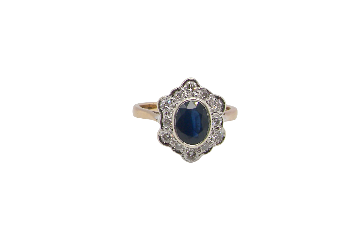 A 9 carat gold cluster ring that features an inky black blue oval cut sapphire. This measures 8x6mm in a safe rim style setting