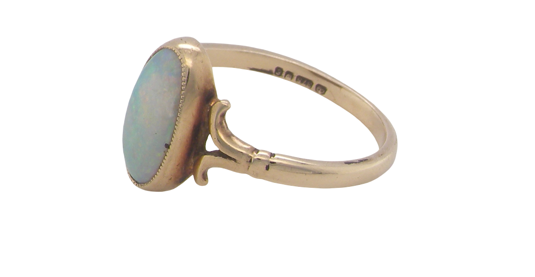A 9 carat gold dress ring that features an oval shaped opal. Measures 12x6.7mm, with a very good play of colour across the white background. Mille grain setting
side angle