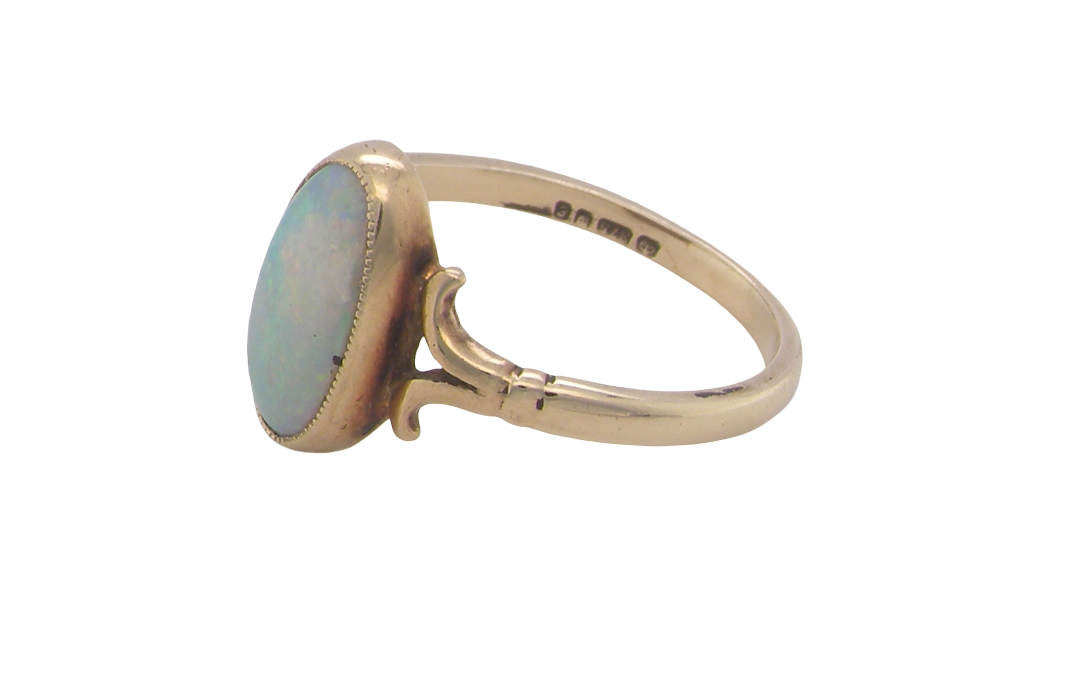 A 9 carat gold dress ring that features an oval shaped opal. Measures 12x6.7mm, with a very good play of colour across the white background. Mille grain setting
side angle