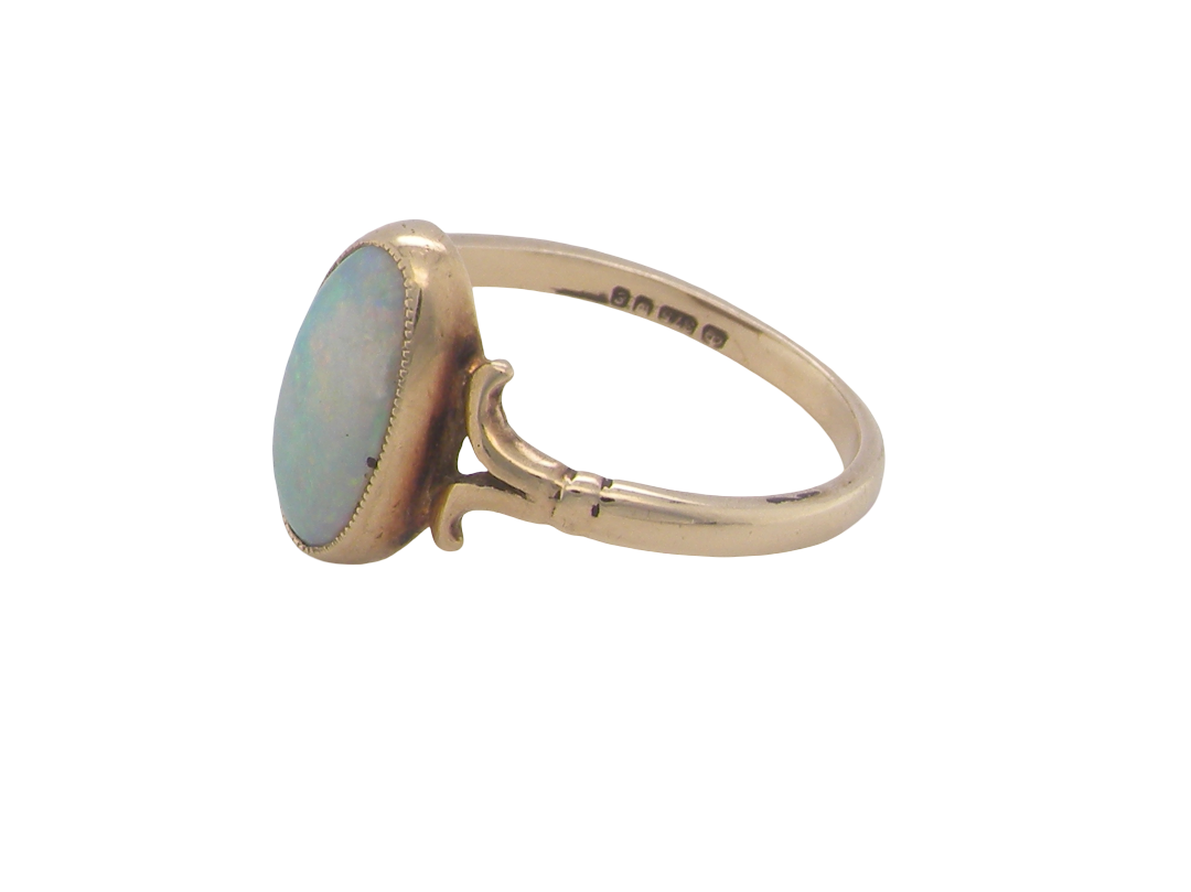 A 9 carat gold dress ring that features an oval shaped opal. Measures 12x6.7mm, with a very good play of colour across the white background. Mille grain setting
side angle