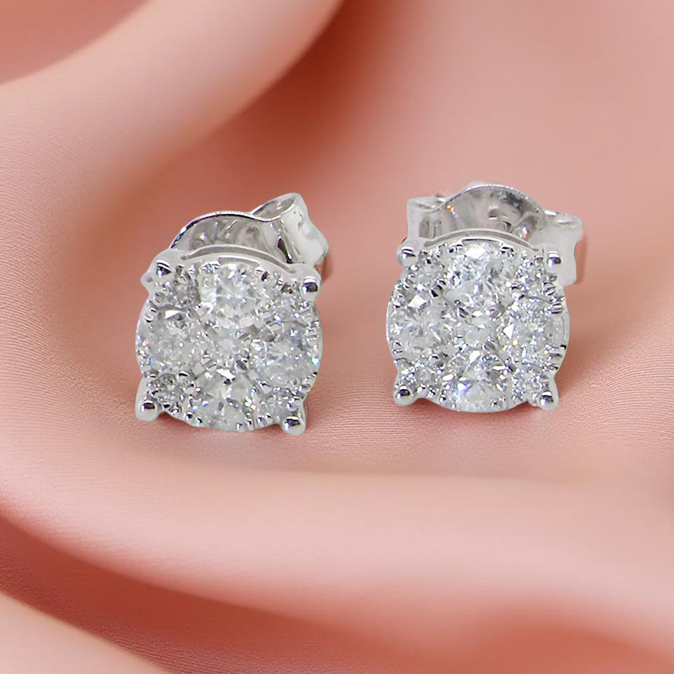 Diamond stud earrings on a person's ear with a soft pink background