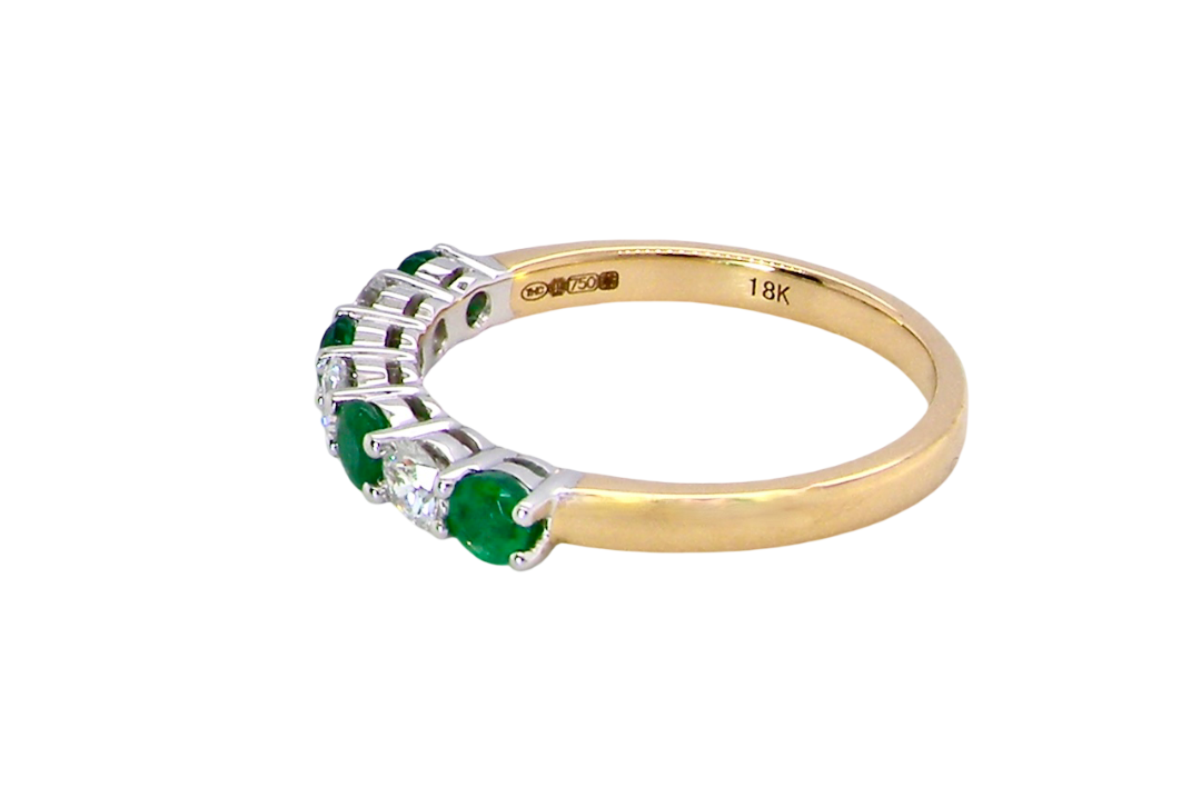 A NEW seven stone half hoop eternity ring. Set with four round emeralds, each 2.8mm (