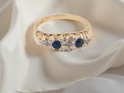 Gold ring with blue and clear gemstones on a white fabric background