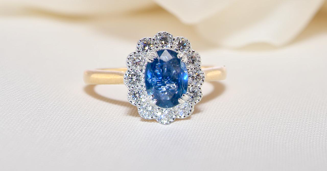 A beautiful cluster ring featuring an oval-cut mid to dark blue sapphire measuring 7 × 5 mm