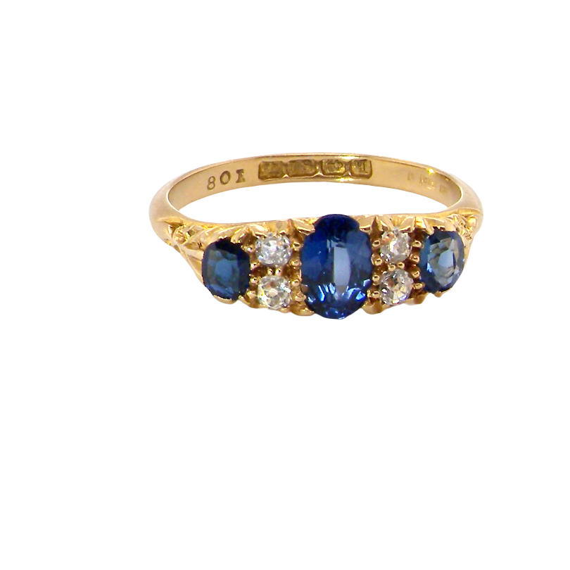 A yellow gold ring featuring a central oval blue sapphire flanked by round and oval blue sapphires and small clear diamonds, shown on a plain white background.