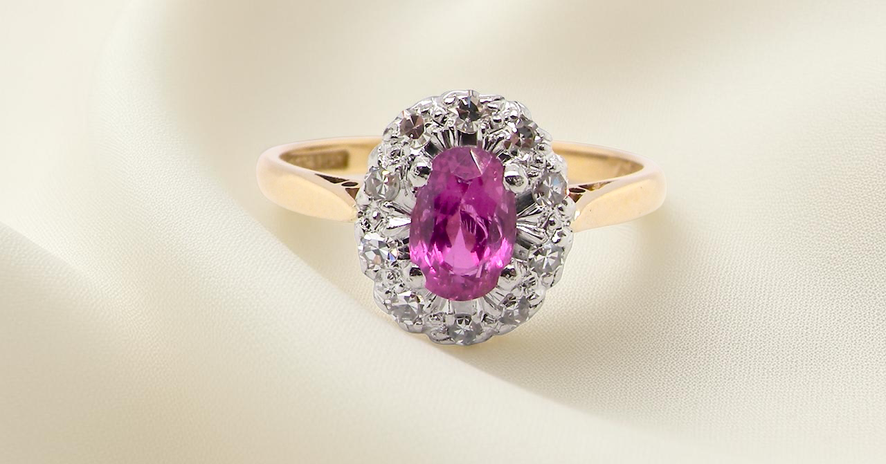 A beautiful vintage cluster ring showcasing a vivid pink sapphire centre stone, measuring approximately 6.6 × 4.3 mm