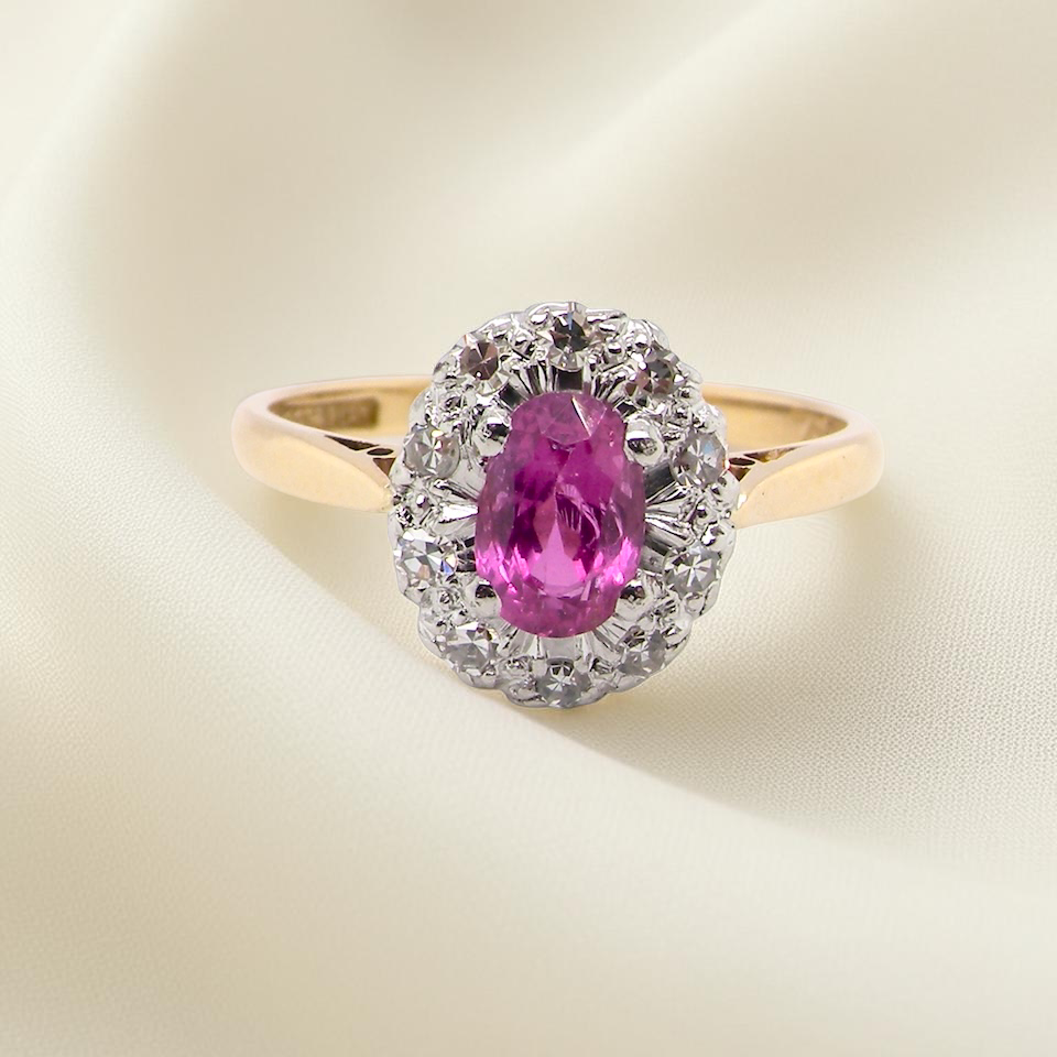 A beautiful vintage cluster ring showcasing a vivid pink sapphire centre stone, measuring approximately 6.6 × 4.3 mm