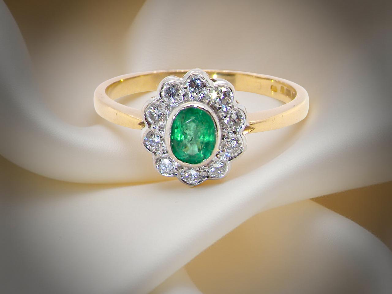 A beautifully elegant cluster ring featuring a central oval-cut emerald, measuring 5 x 4mm