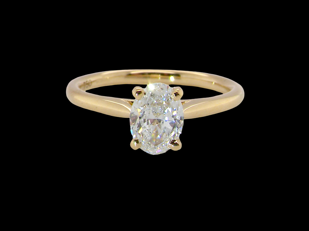 A yellow gold solitaire ring featuring an oval-cut diamond set in a four-prong setting, presented on a solid black background.