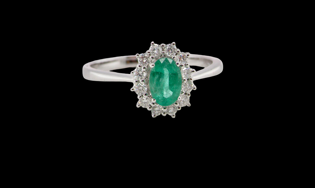 A classic cluster ring set with an oval cut emerald centre stone, measures 6x4mm, grass green colour.
Complimented by an outer halo of twelve brilliant cut white diamonds,