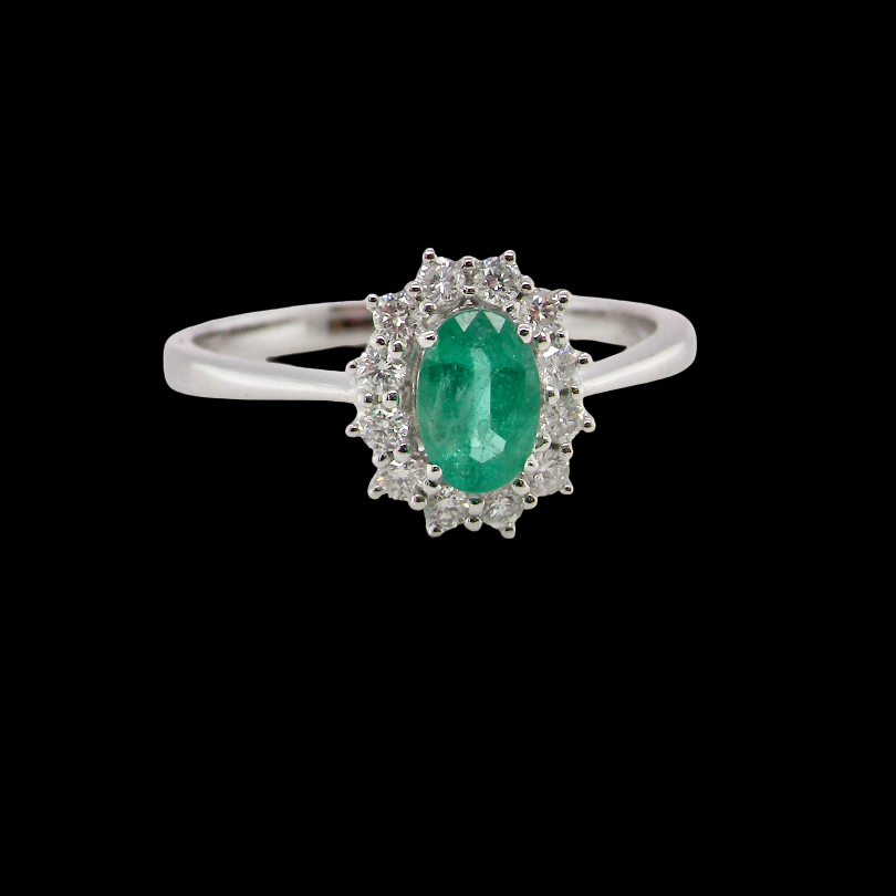 A classic cluster ring set with an oval cut emerald centre stone, measures 6x4mm, grass green colour.
Complimented by an outer halo of twelve brilliant cut white diamonds,