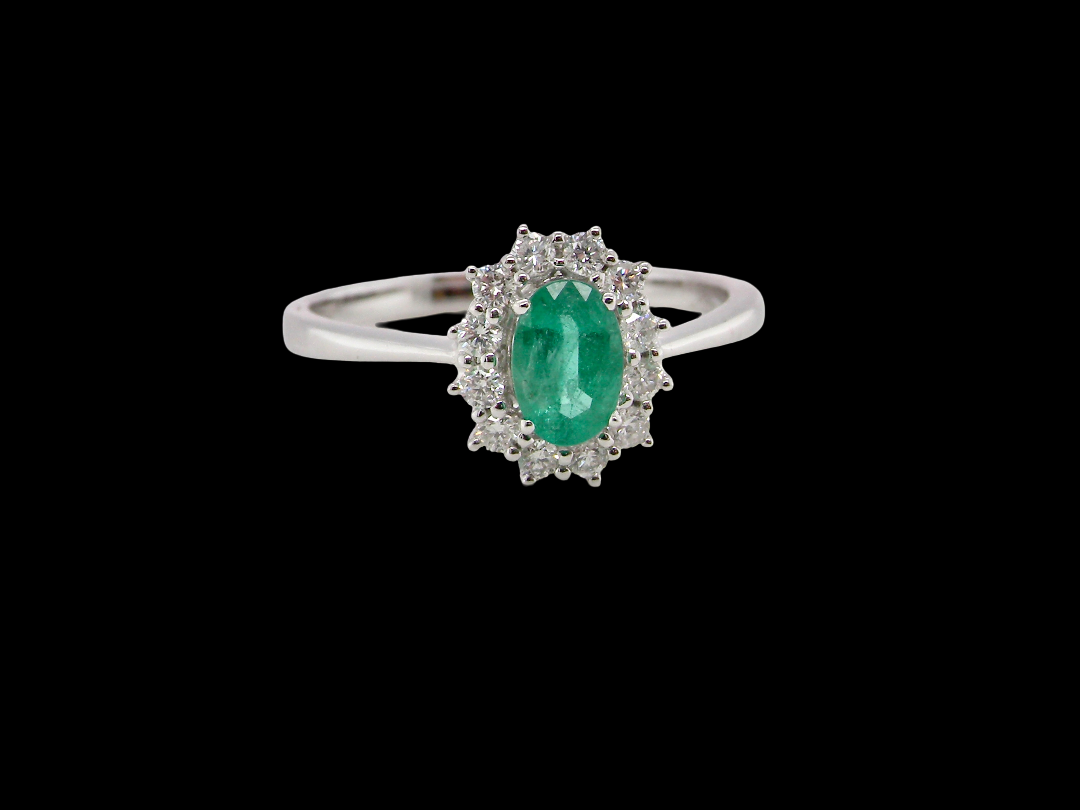 A classic cluster ring set with an oval cut emerald centre stone, measures 6x4mm, grass green colour.
Complimented by an outer halo of twelve brilliant cut white diamonds,