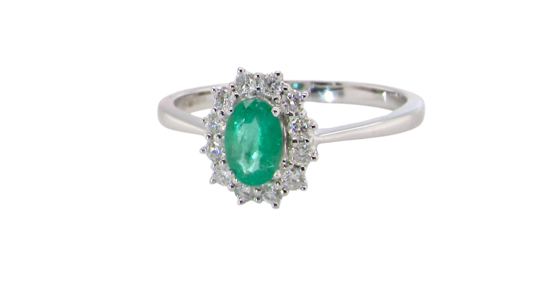 A classic cluster ring set with an oval cut emerald centre stone, measures 6x4mm, grass green colour.
Complimented by an outer halo of twelve brilliant cut white diamonds, each 1.7mm