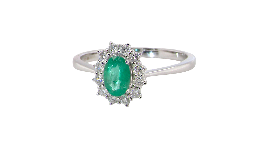 A classic cluster ring set with an oval cut emerald centre stone, measures 6x4mm, grass green colour.
Complimented by an outer halo of twelve brilliant cut white diamonds, each 1.7mm