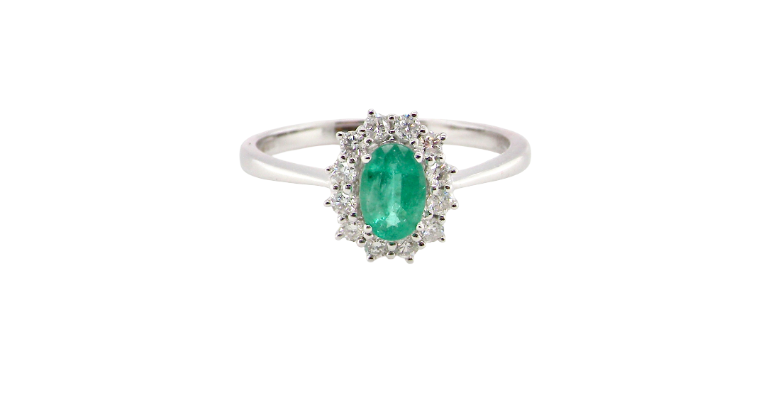 A classic cluster ring set with an oval cut emerald centre stone, measures 6x4mm, grass green colour.
Complimented by an outer halo of twelve brilliant cut white diamonds, each 1.7mm (total est at 0.25 carats)