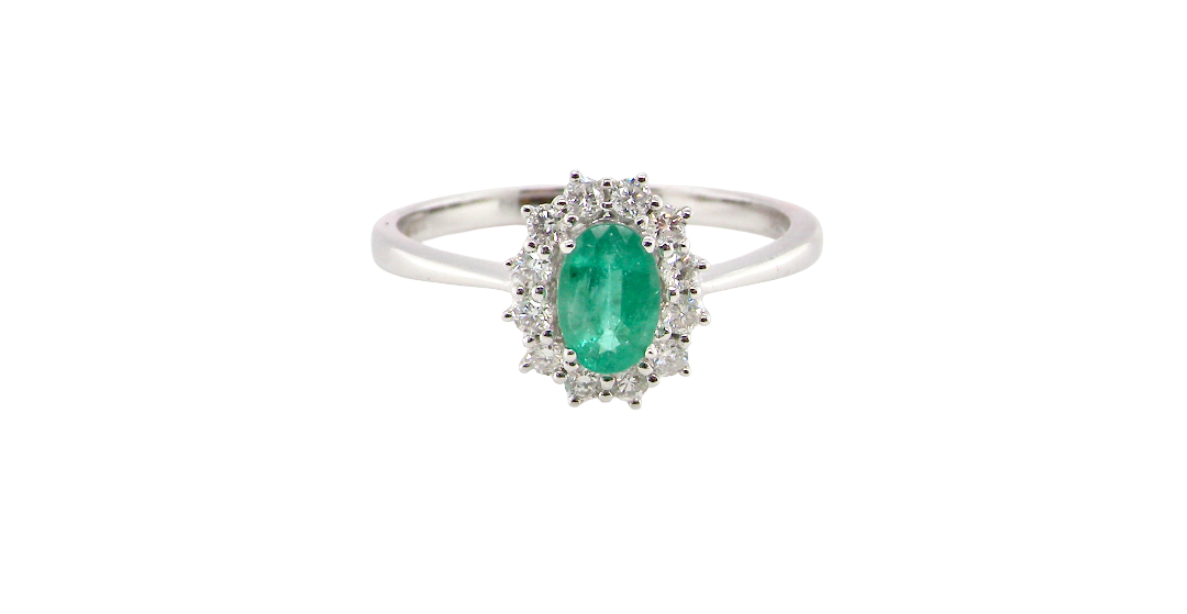 A classic cluster ring set with an oval cut emerald centre stone, measures 6x4mm, grass green colour.
Complimented by an outer halo of twelve brilliant cut white diamonds, each 1.7mm (total est at 0.25 carats)