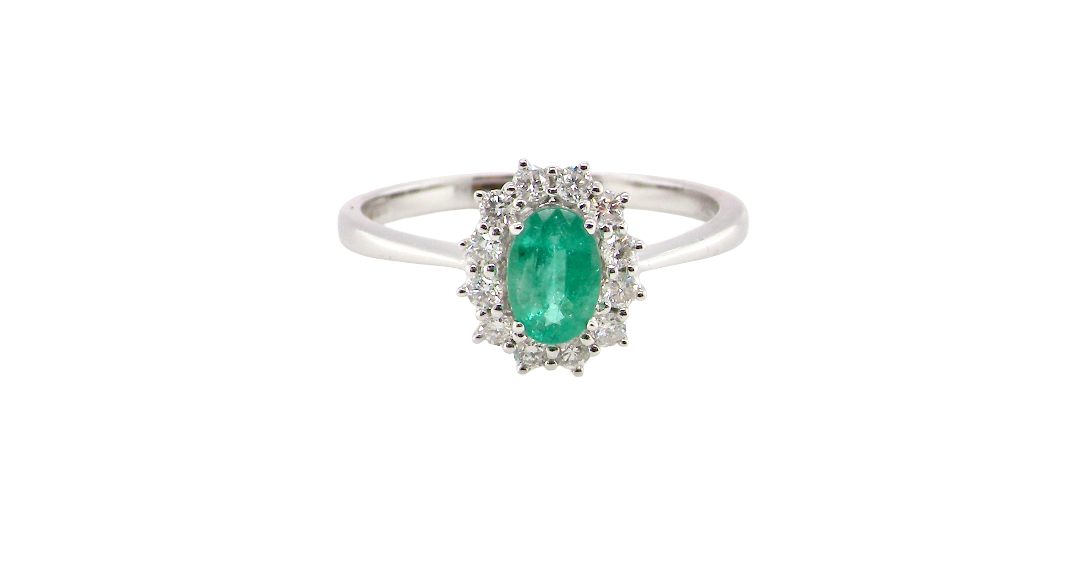 A classic cluster ring set with an oval cut emerald centre stone, measures 6x4mm, grass green colour.
Complimented by an outer halo of twelve brilliant cut white diamonds, each 1.7mm (total est at 0.25 carats)