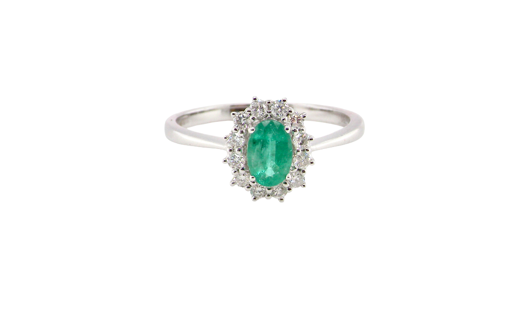 A classic cluster ring set with an oval cut emerald centre stone, measures 6x4mm, grass green colour.
Complimented by an outer halo of twelve brilliant cut white diamonds, each 1.7mm (total est at 0.25 carats)