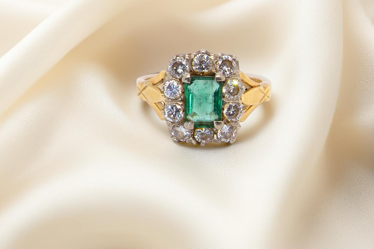 A cluster ring that features a rectangular emerald centre stone, 7x5mm . Deep green colour,