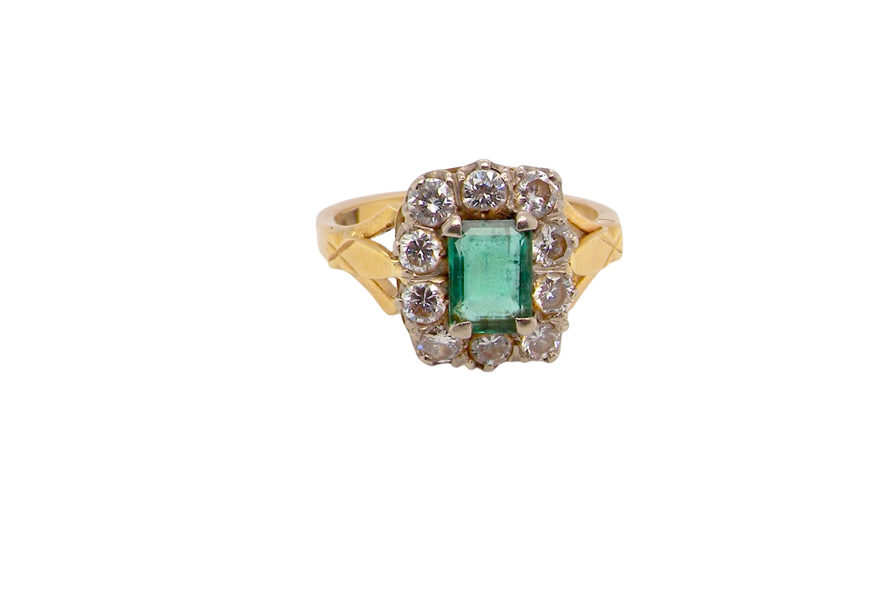 A cluster ring that features a rectangular emerald centre stone, 7x5mm . Deep green colour, natural inclusions that can be seen under an eye glass,