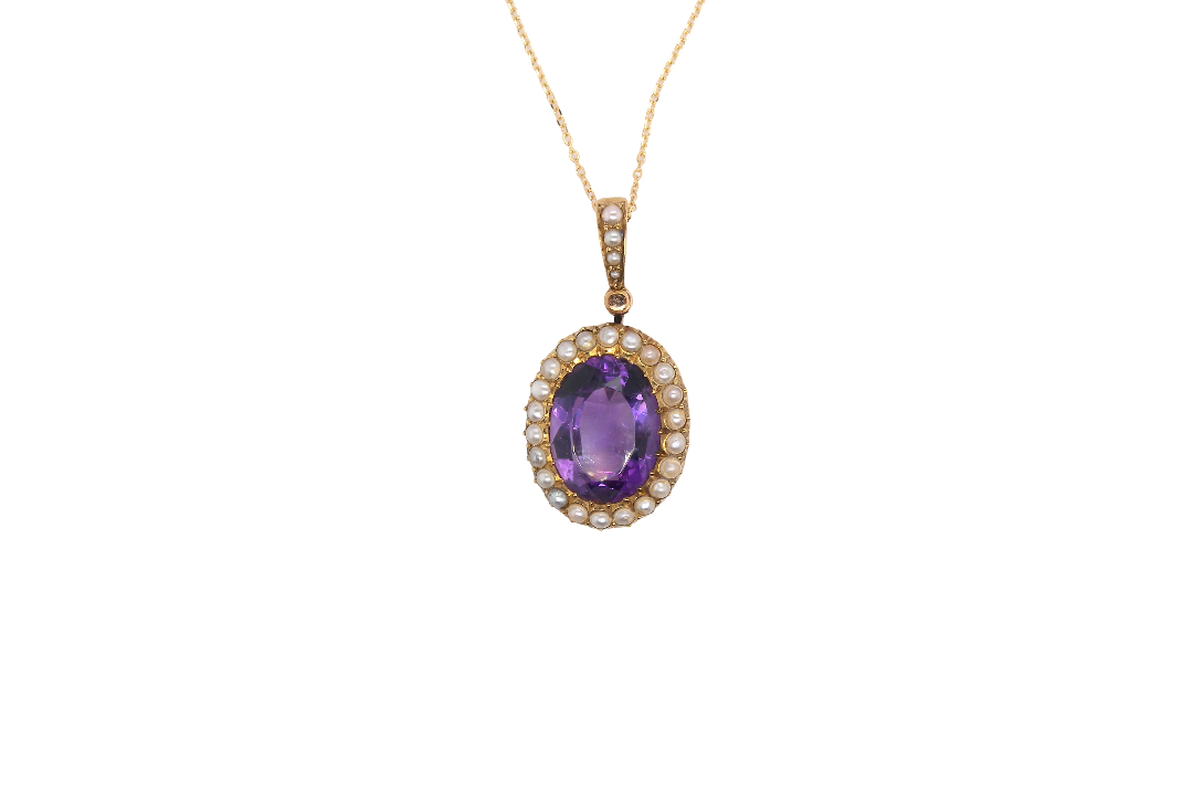 An oval pendant necklace featuring a central purple amethyst gemstone surrounded by a halo of small clear stones, set in yellow gold and suspended from a delicate gold chain against a plain white background.