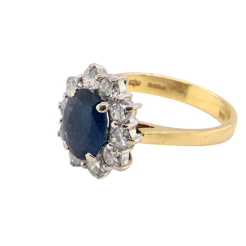 A yellow gold ring featuring a central oval dark blue sapphire surrounded by a halo of clear diamonds, set on a plain white background.