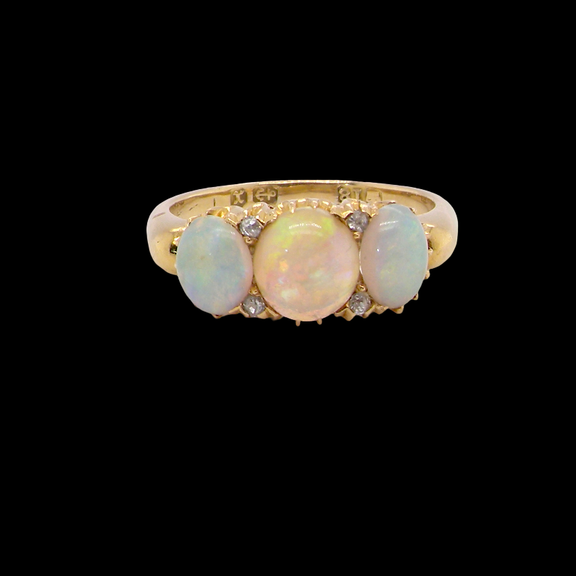 A yellow gold ring featuring three oval opal stones in a row, accented by small clear stones on a solid black background.