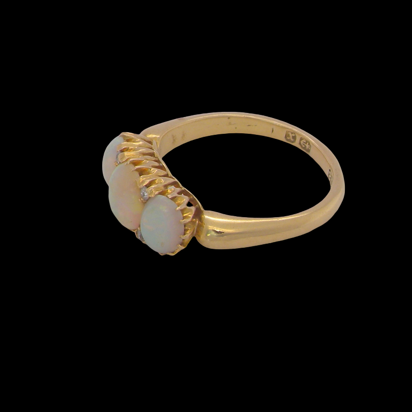 A yellow gold ring featuring three oval cabochon opal gemstones in a textured bezel setting, shown against a solid black background.