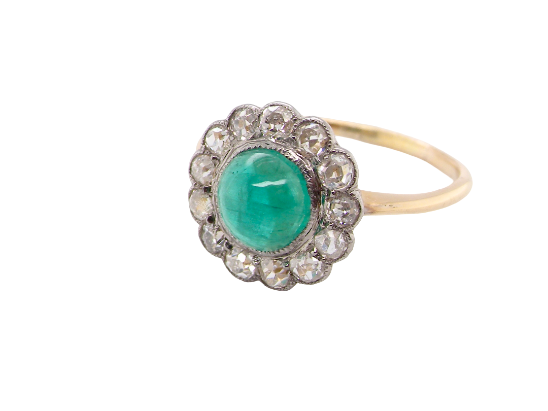 An antique-style ring featuring a round green emerald-cut center stone surrounded by a halo of small clear stones, set on a yellow gold band.