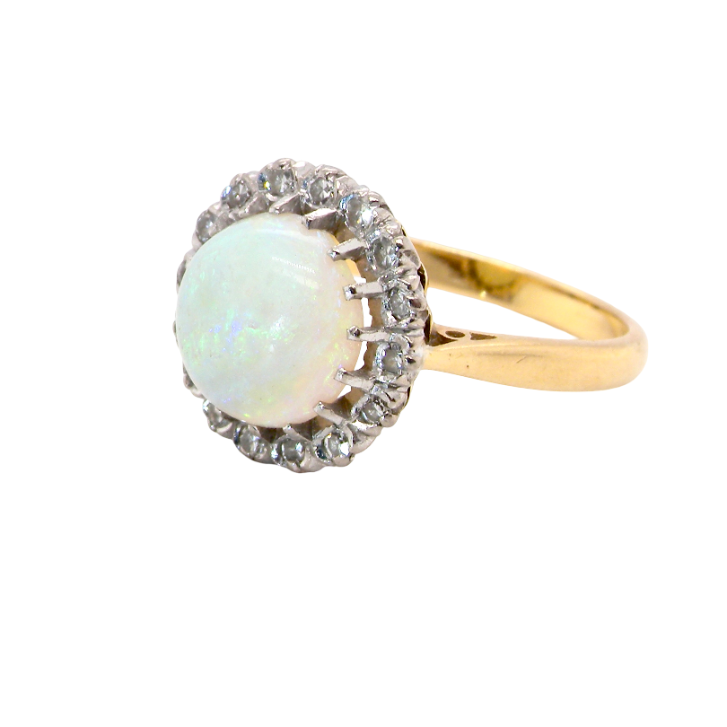 A yellow gold ring featuring a round white opal surrounded by a halo of small clear stones, set against a plain white background.