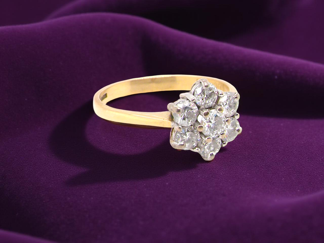 Gold ring with diamond cluster on a purple fabric background
