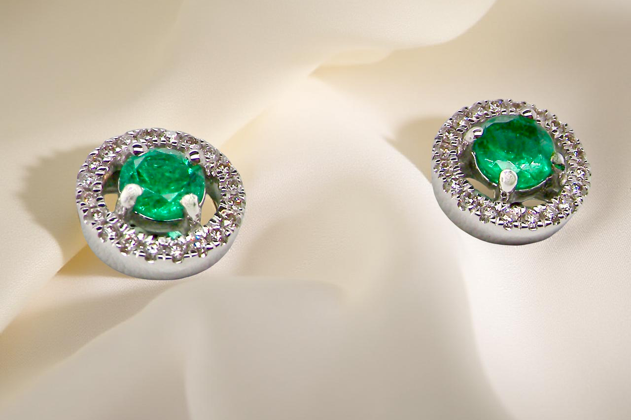 Pair of emerald earrings with diamond accents on a light background