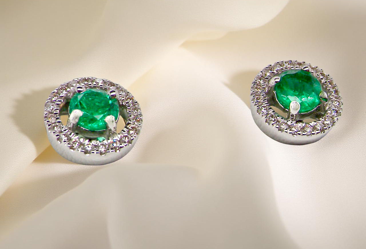 Pair of emerald earrings with diamond accents on a light background