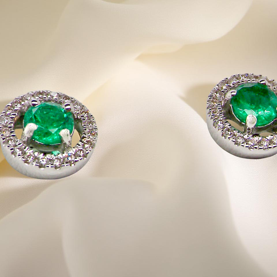 Pair of emerald earrings with diamond accents on a light background