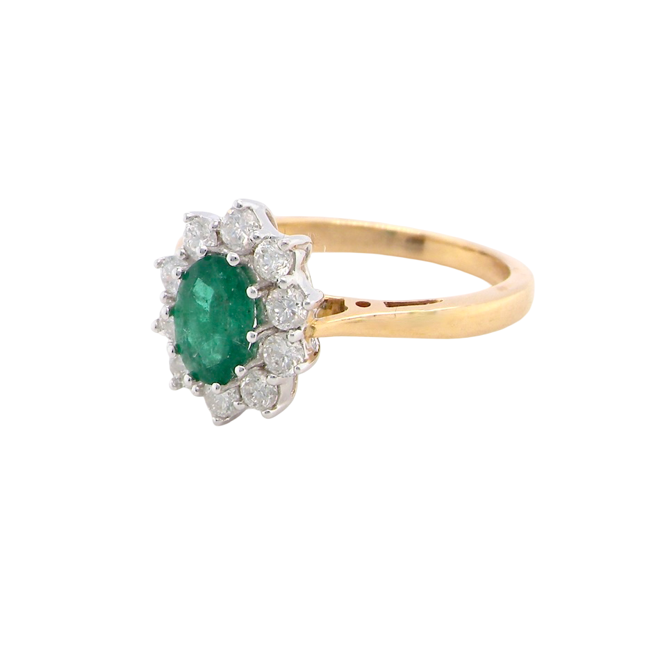 A fine traditional emerald and diamond cluster ring, featuring a vibrant oval-cut emerald to the centre measuring approximately 7 × 5 mm side
