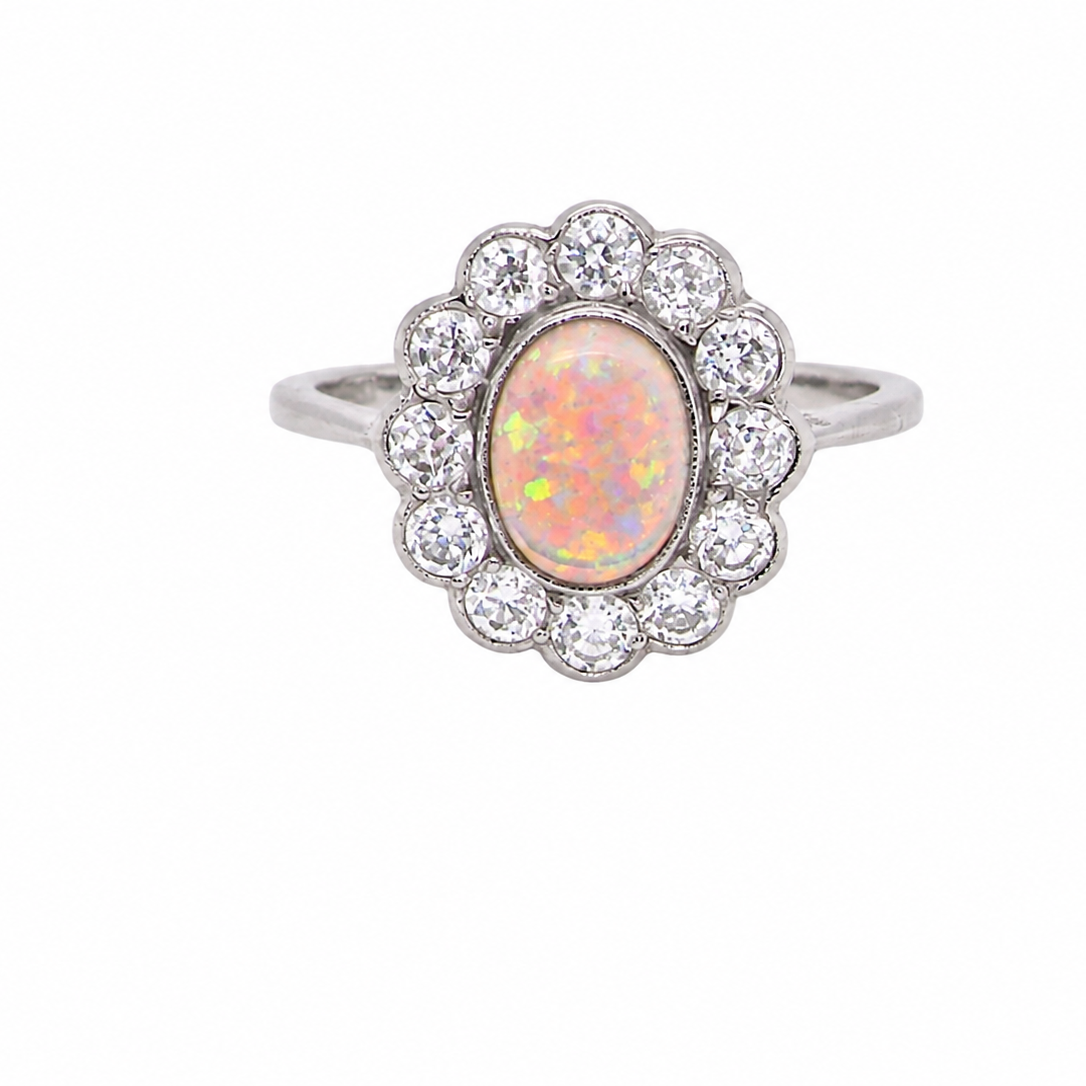 A fine vintage cluster ring. Features to the centre an oval shaped opal, with excellent play of colour, pink to one way, vibrant green to the other with flashes of electric blue also