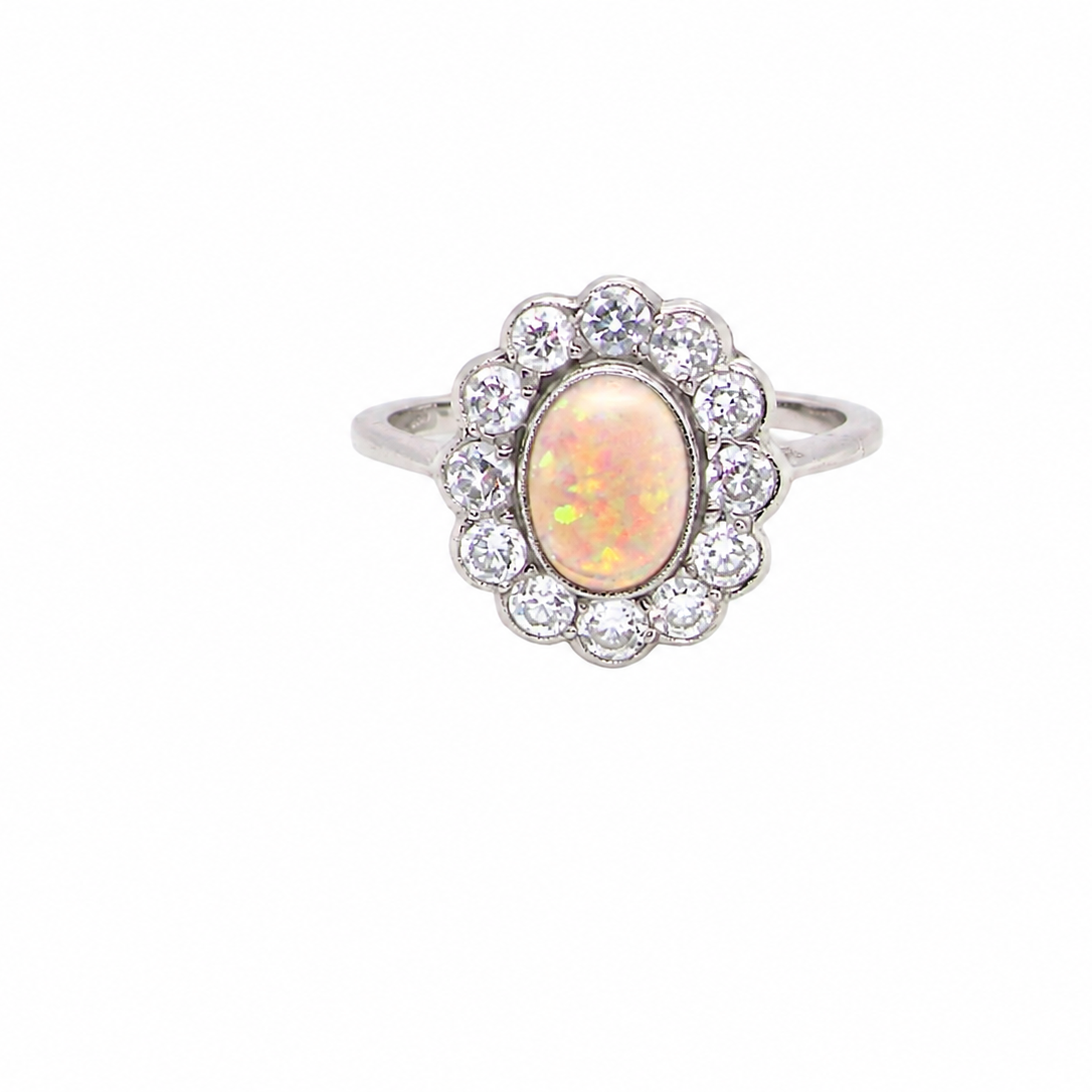 A fine vintage cluster ring. Features to the centre an oval shaped opal, with excellent play of colour, pink to one way, vibrant green to the other with flashes of electric blue also within the body of the gem.