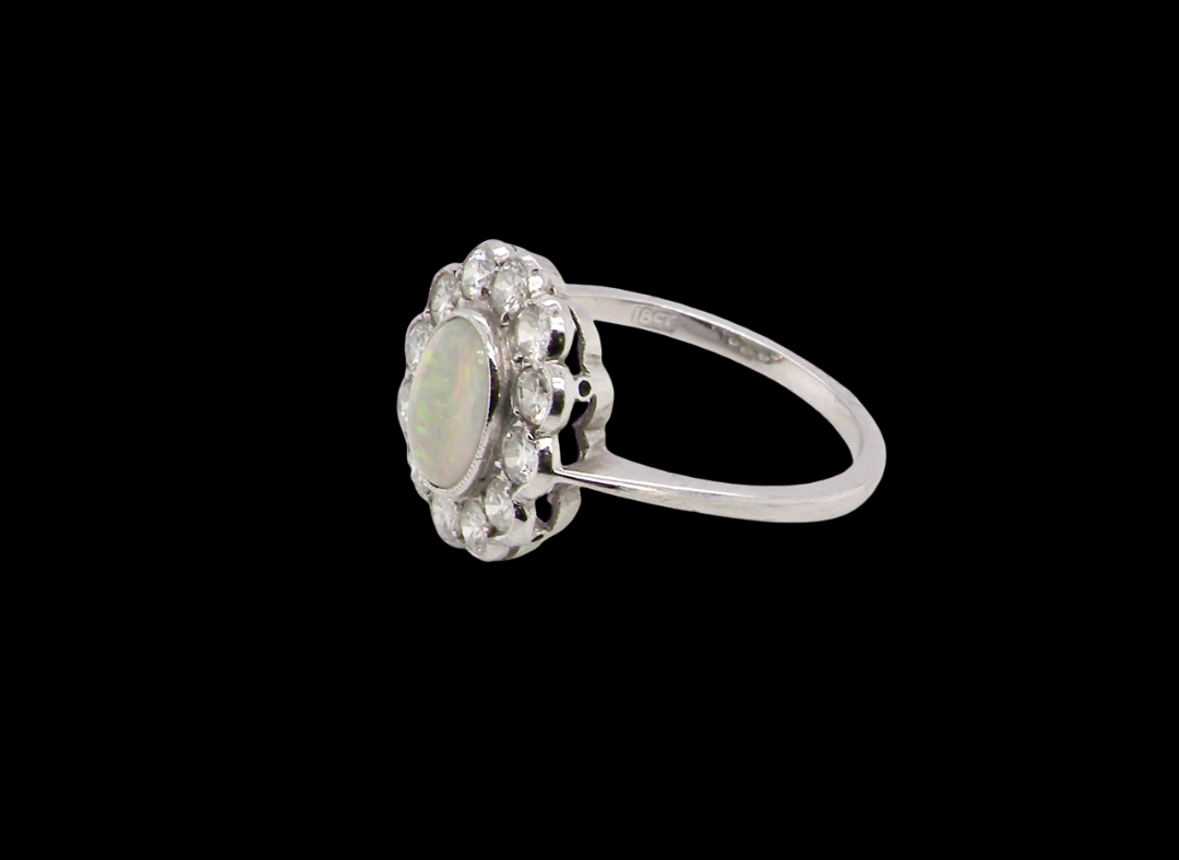 A fine vintage cluster ring. Features to the centre an oval shaped opal, with excellent play of colour, pink to one way, vibrant green to the other with flashes of electric blue also within the body of the gem.
side