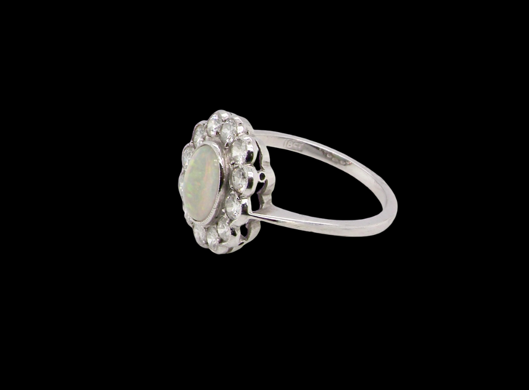A fine vintage cluster ring. Features to the centre an oval shaped opal, with excellent play of colour, pink to one way, vibrant green to the other with flashes of electric blue also within the body of the gem.
side