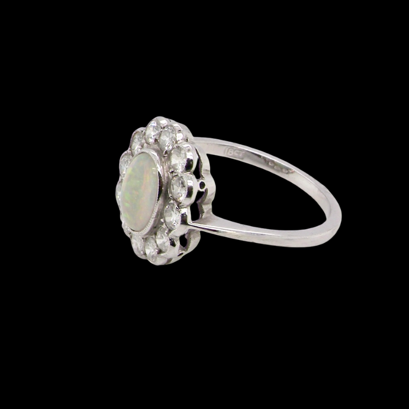 A fine vintage cluster ring. Features to the centre an oval shaped opal, with excellent play of colour, pink to one way, vibrant green to the other with flashes of electric blue also within the body of the gem.
side