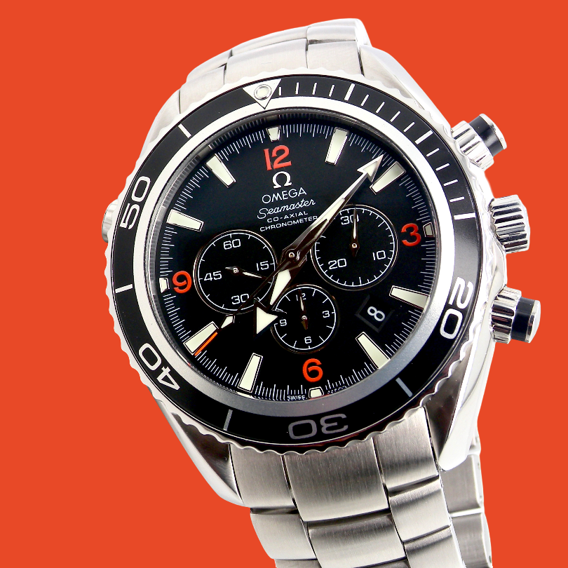 Omega x Swatch Chassis Automatic watch with a black dial, silver stainless steel case and bracelet, and orange accents, set against a solid orange background.