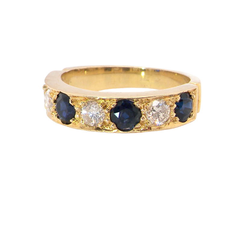 A yellow gold eternity ring featuring alternating round dark blue sapphires and clear round diamonds, shown on a plain white background.