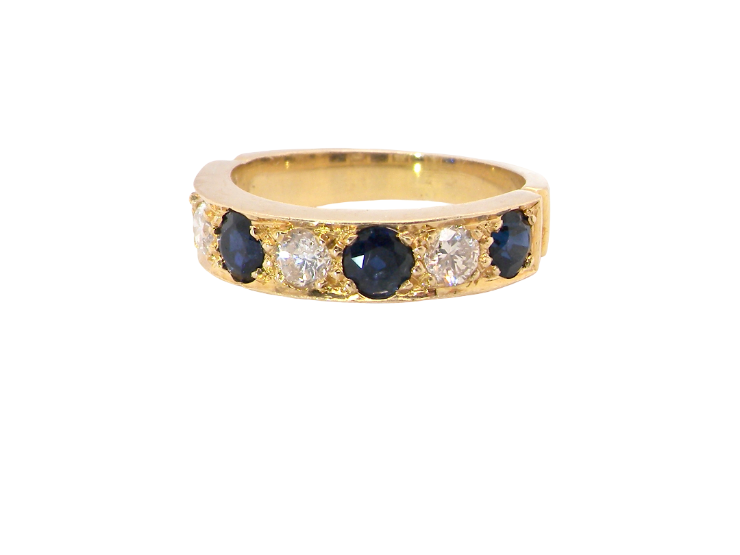 A yellow gold eternity ring featuring alternating round dark blue sapphires and clear round diamonds, shown on a plain white background.