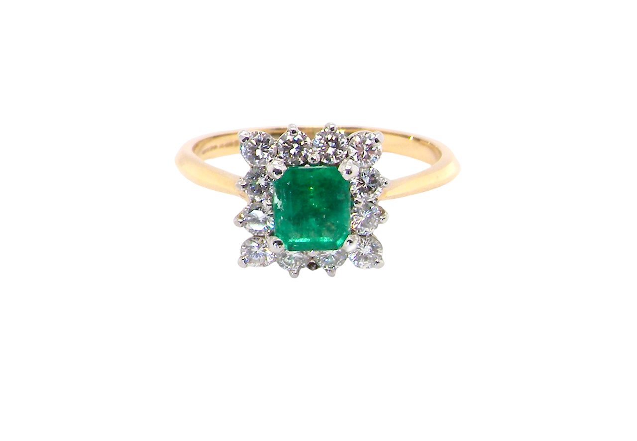 A lovely cluster ring that features to the centre a rectangle shaped emerald, 7x5mm. Shows a deep grass green colour which does have natural inclusions common with most emeralds,