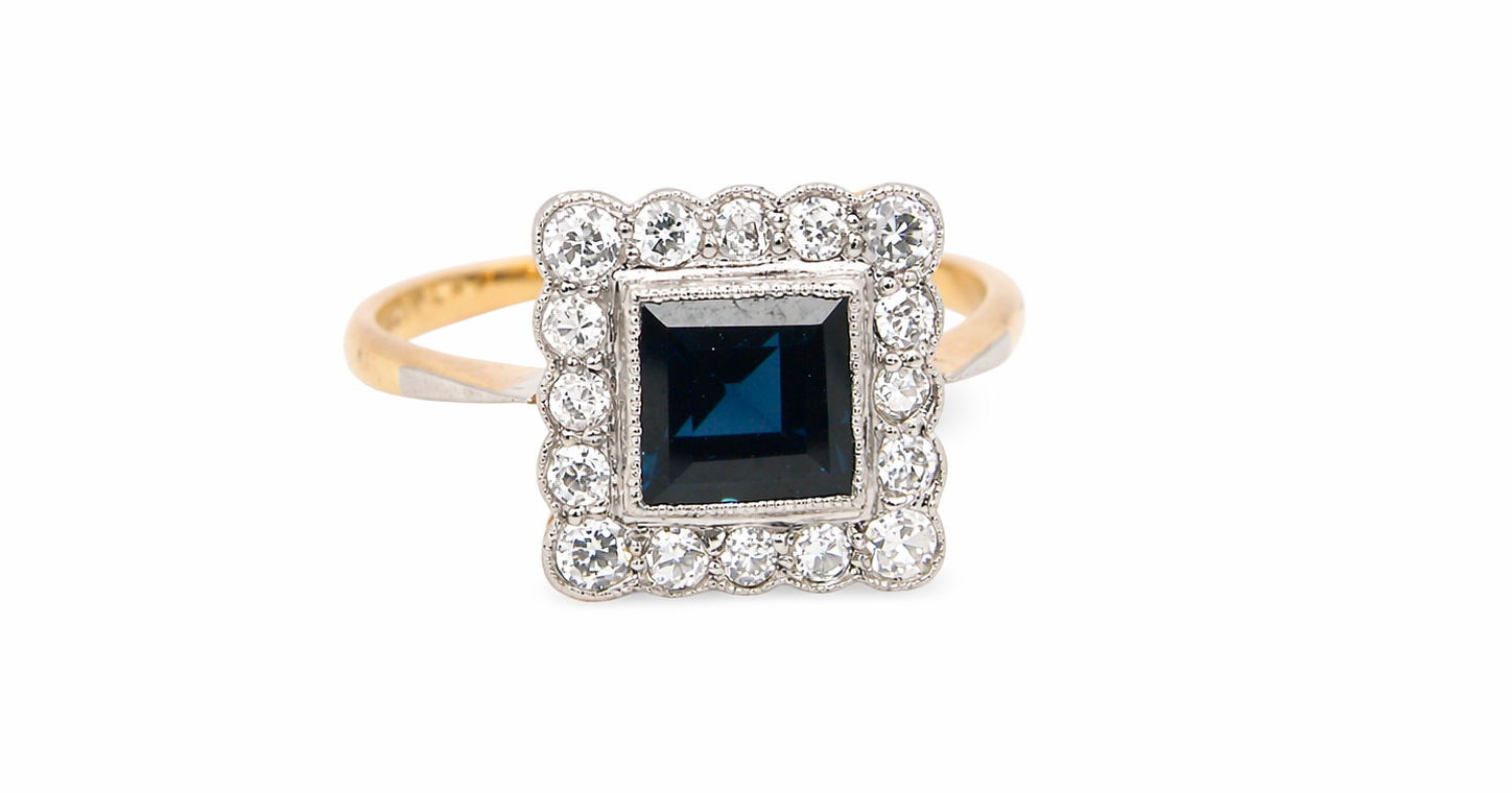 A mid 20th century cluster ring. Features a square dark blue sapphire 5x5mm (est 0.60 carats) mille grain setting in platinum. 