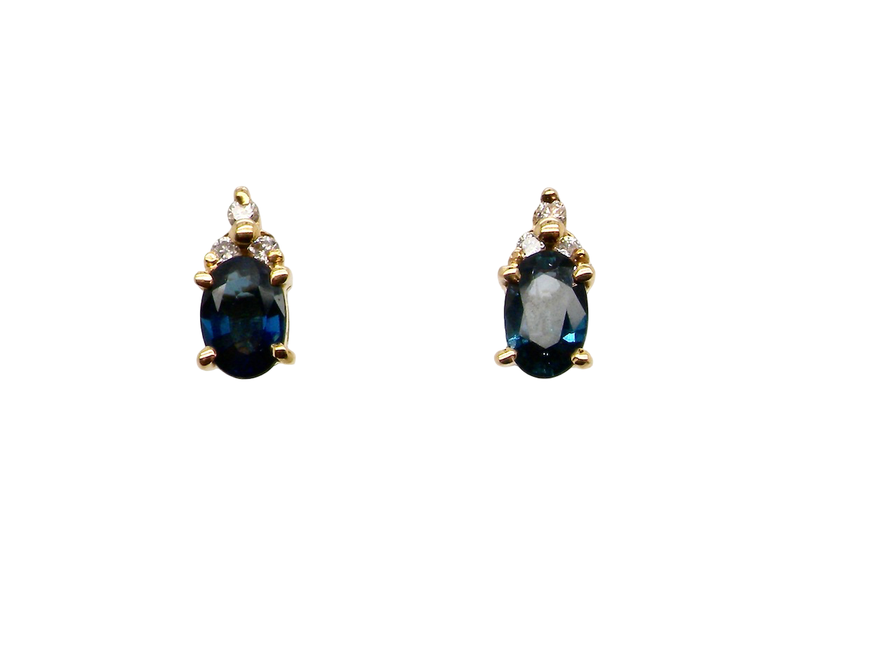A pair of 18 carat gold earrings*. Set with a dark blue oval cut sapphire 6x4mm, claw set.
Above each, three small white diamonds, overall size 9x4.6mm, weight each 1 gram.